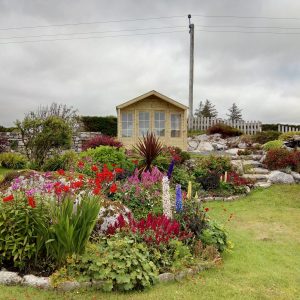 MCD Garden Sheds in a Garden With flowers. Grey Clouds cover the sky